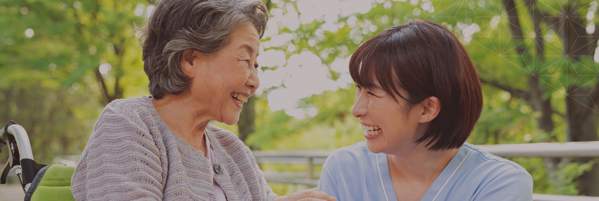 庭園で職員と入居者が談笑する様子。自然光に恵まれた明るい雰囲気。